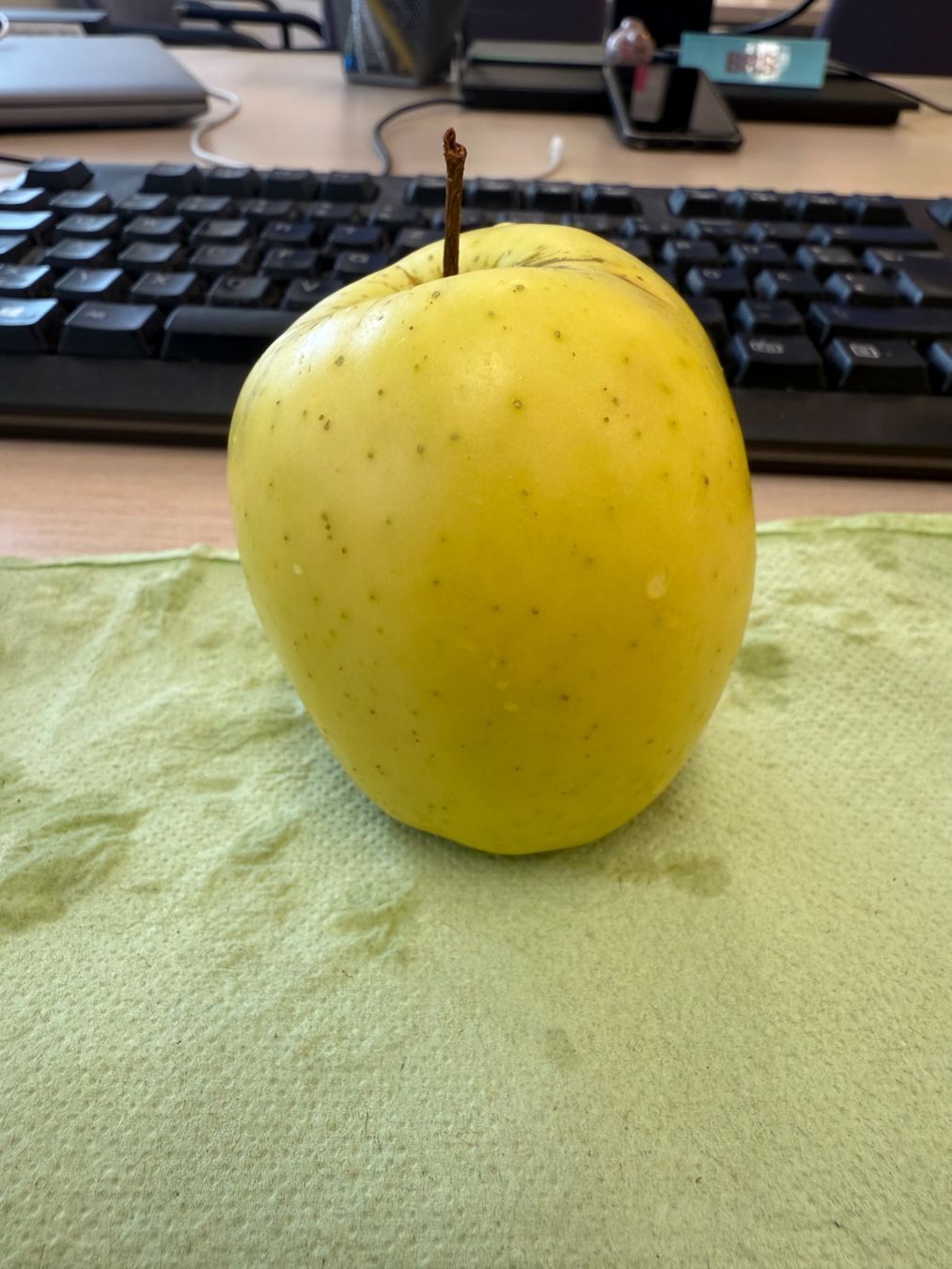 Apfel auf grünem Papier liegend auf einem Schreibtisch. Dahinter eine Tastatur.